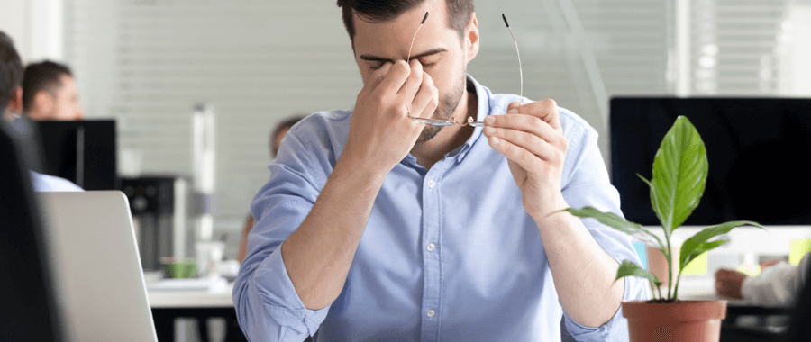 man sitting on his office chair, holding his head in pain