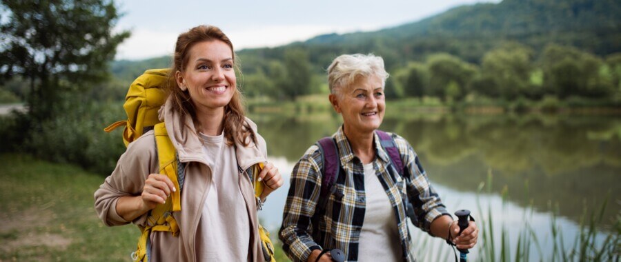 Happy, healthy senior woman with trekking poles and companion hiking