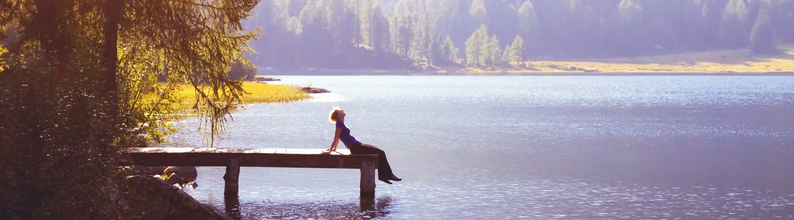 Woman sits in the sun on lake dock.