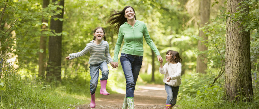 Woman walks through nature holding hands with her children.