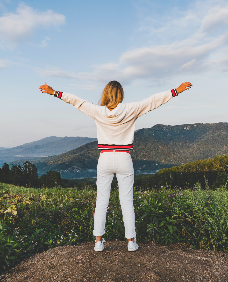 Woman stretches arms while overlooking ocean.