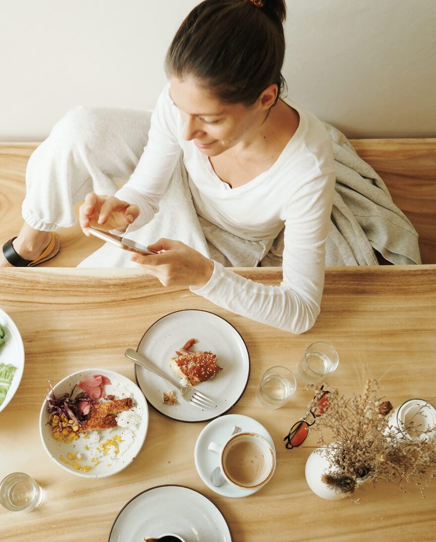Woman checks phone with lunch on the table before her.