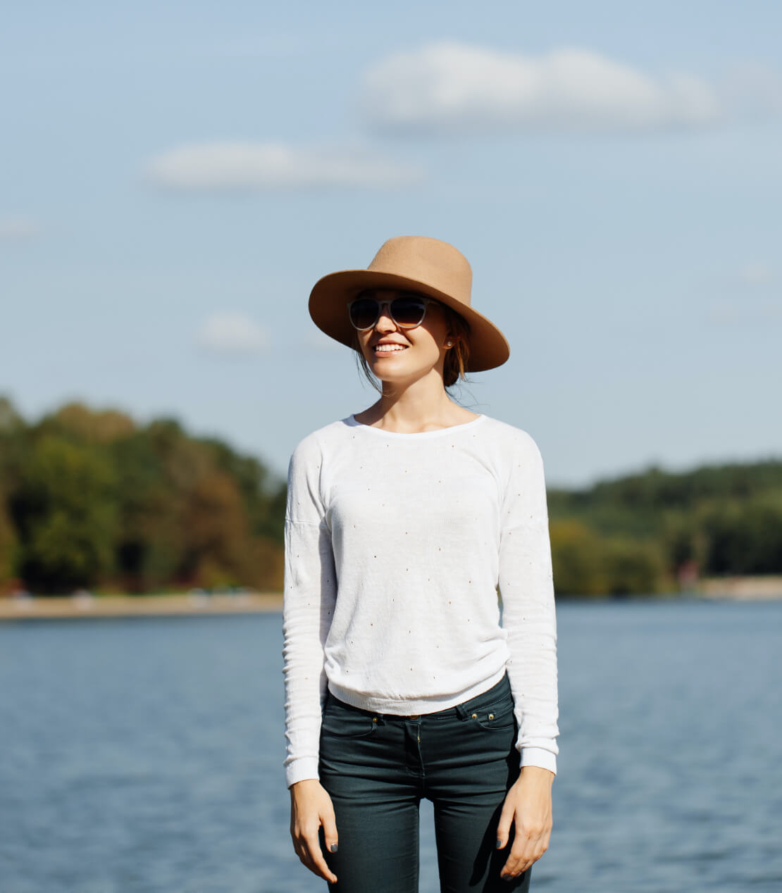Woman with hat and sunglasses in front of lake.