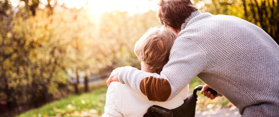 Man hugging woman with guillain-barre syndrome in wheelchair at park in fall